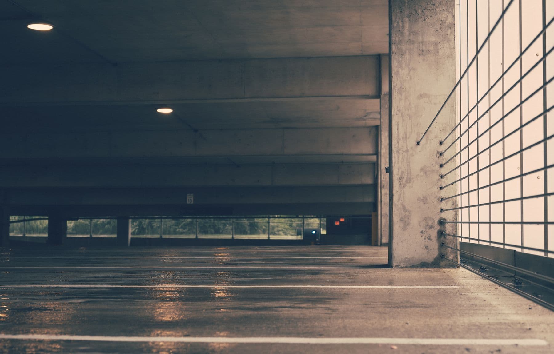 An empty, dim parking garage level with a wet concrete floor and a metal screen wall.