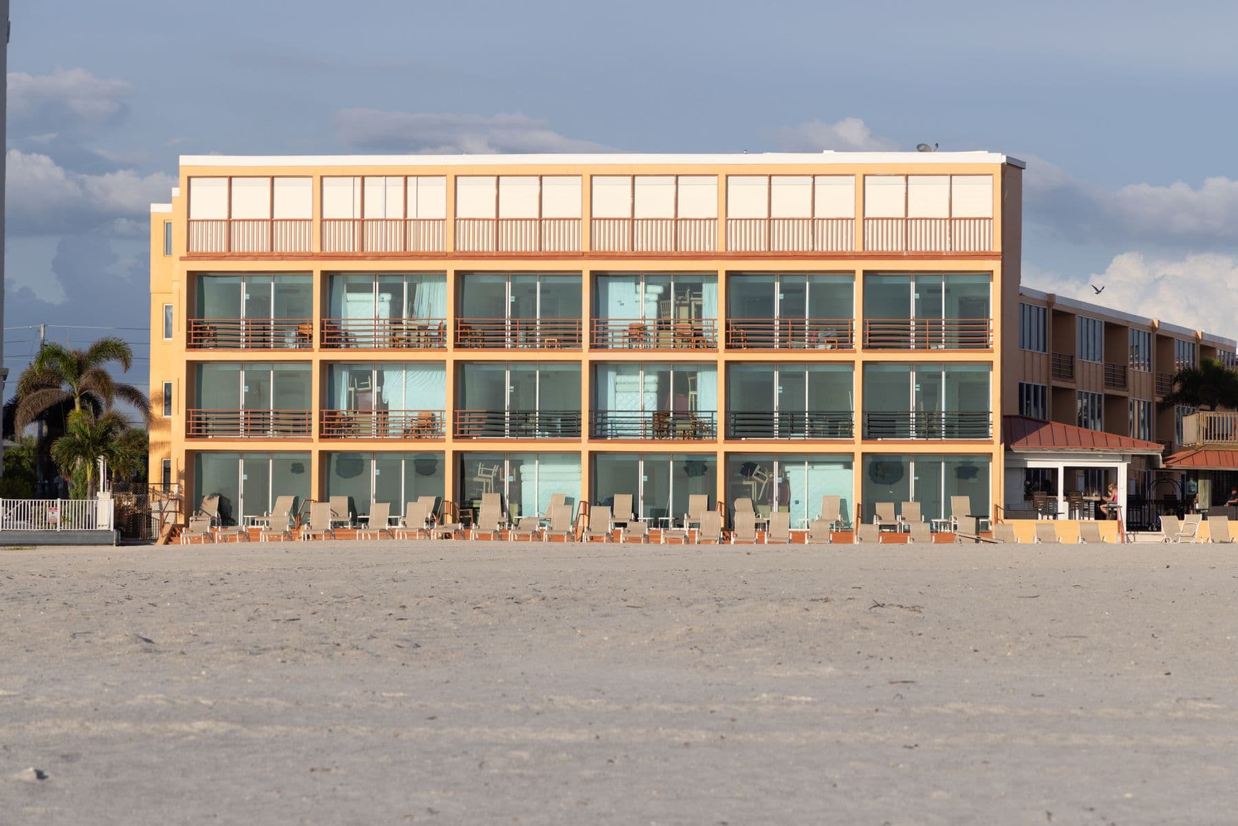A three-story beachfront building with balconies and orange trim, seen across the sand.