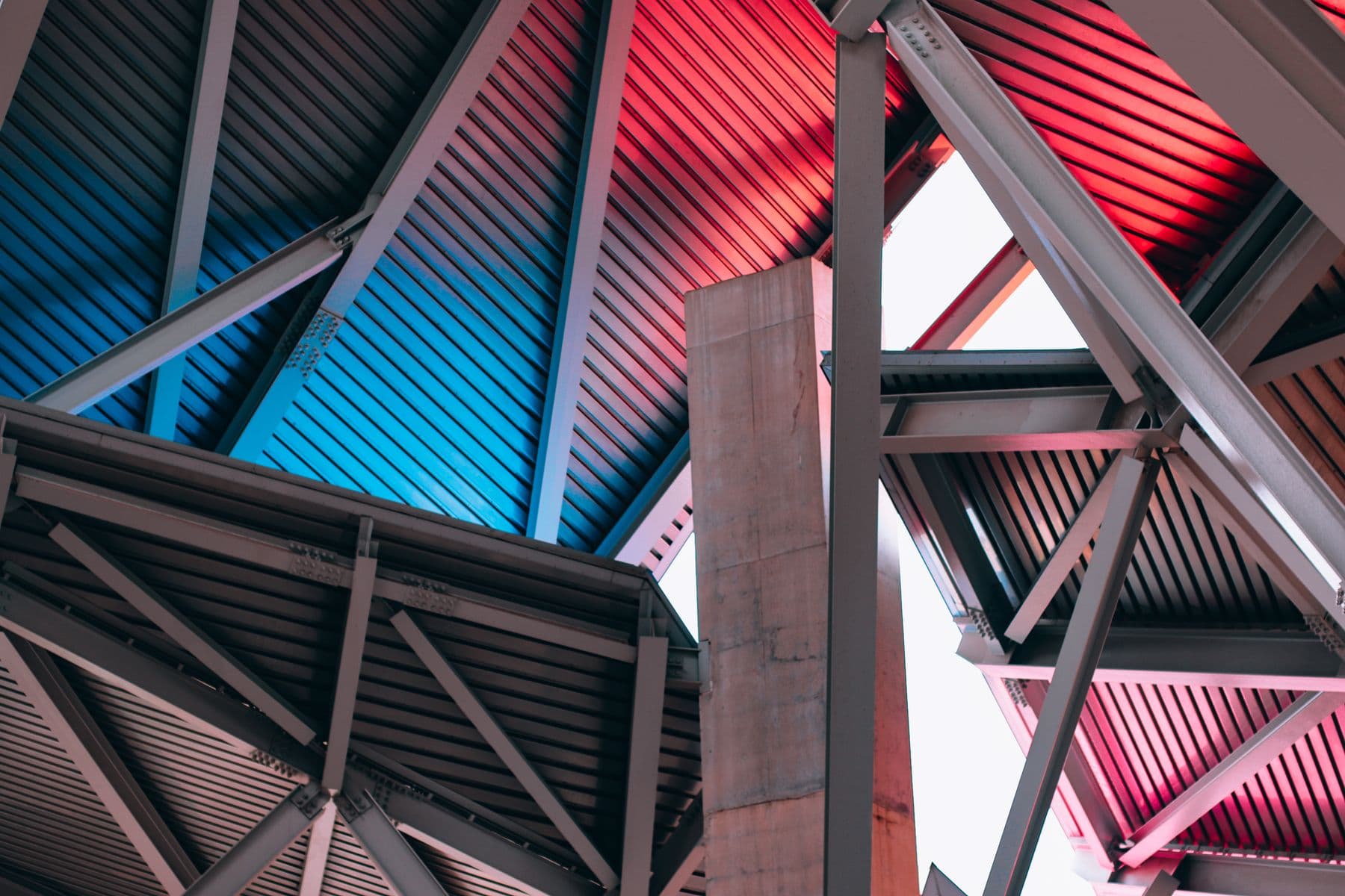 Steel beams and roof framing painted in red, blue and gray, seen from below.