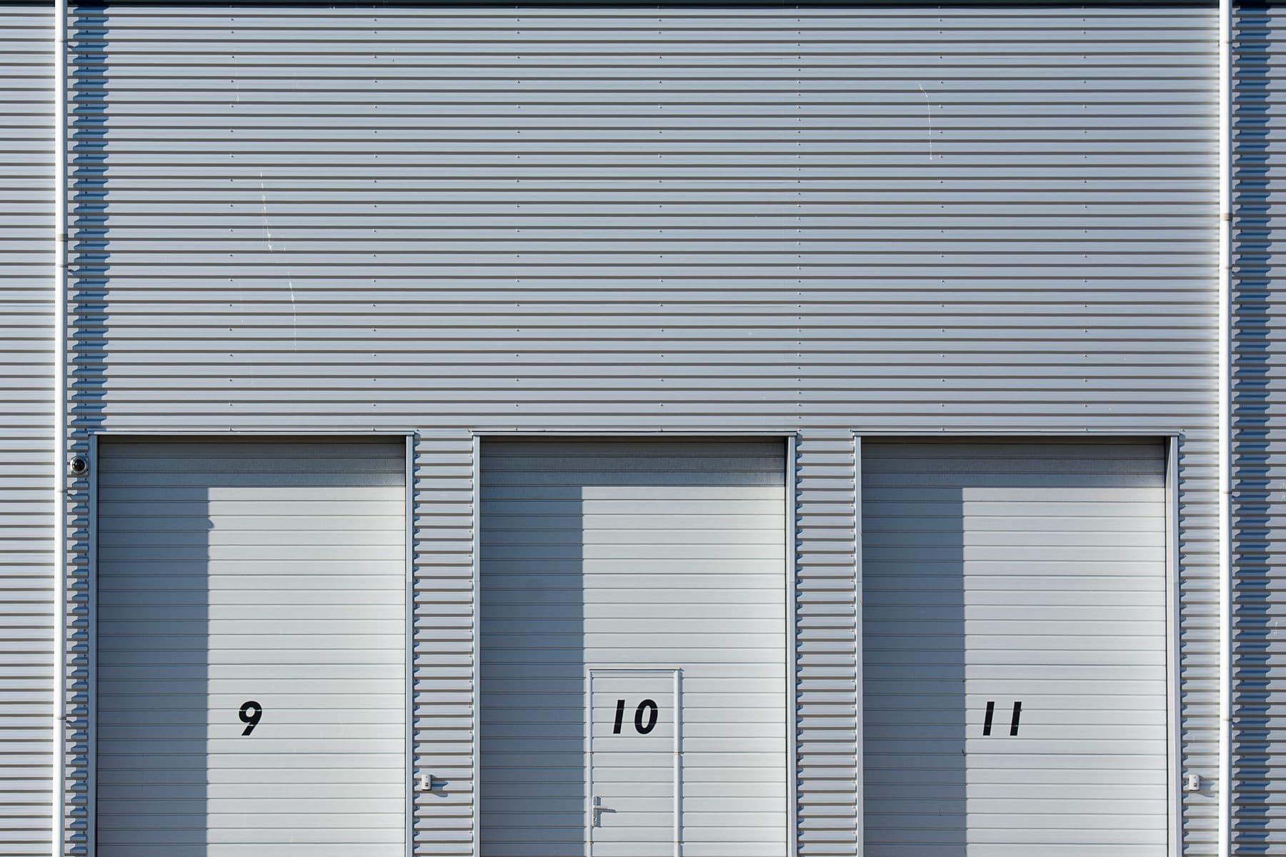Three numbered roll-up doors in the gray metal wall of an industrial building.